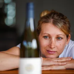 Eine Frau betrachtet aufmerksam eine Flasche Wein. Sie wirkt nachdenklich und interessiert.