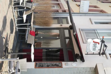 Ein kleines Bistro mit einer einladenden Eingangstür und Stühlen draußen. Die Atmosphäre ist gemütlich und einladend.