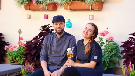 Ein fröhliches Paar sitzt in einem Garten mit bunten Blumen. Sie lachen und genießen ein Getränk.