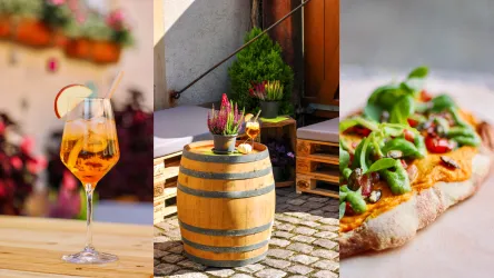 Ein erfrischendes Getränk in einem Glas, ein Holztisch mit einem dekorativen Holzfass und wunderschönem Flair, sowie eine köstliche Pizza mit frischen Zutaten. Eine einladende Atmosphäre für entspannte Momente.