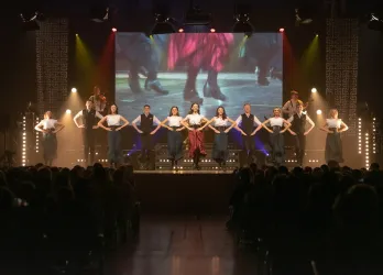 Eine eindrucksvolle Bühnenshow mit Tänzern in traditionellen Kostümen. Im Hintergrund ist ein großes Bild zu sehen, das die Performance ergänzt.