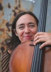 Eine Musikerin lächelt glücklicherweise und hält ihr Cello fest. Der Hintergrund ist rustikal und verleiht der Szene eine besondere Atmosphäre.