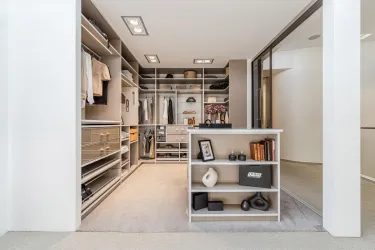 Ein moderner Kleiderschrank mit vielen Regalen und ordentlich aufgehängter Kleidung. In der Mitte steht ein Tisch mit Dekorationsobjekten und Büchern.