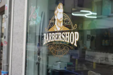 Ein Schaufenster eines Barbierladens mit einem stilvollen Logo. Das Logo zeigt einen bärtigen Mann und den Schriftzug "BARBERSHOP".
