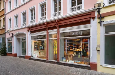 Ein gemütlicher Buchladen mit großen Fenstern in einer ruhigen Straße. Der Außenbereich ist einladend und schön gestaltet.