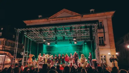 Eine Bühne mit einer Aufführung bei Nacht. Viele Menschen stehen davor und schauen zu, während das Licht grün leuchtet.