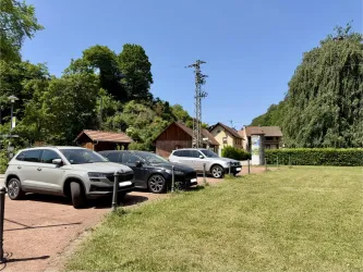 Eine sanierte Parkfläche mit mehreren Autos und umliegendem Grün. Im Hintergrund sind einige Gebäude und Bäume sichtbar.