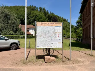 Eine große Wandtafel zeigt eine Wanderkarte des Dahner Felsenlandes. Im Hintergrund sind Bäume und ein Gebäude sichtbar.