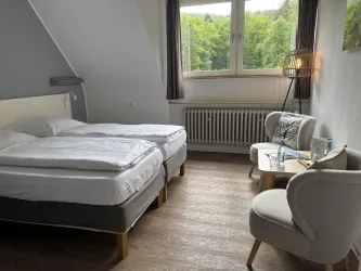 Ein gemütliches Zimmer mit zwei Einzelbetten und modernen Möbeln. Der Blick aus dem Fenster zeigt grünes Laub.