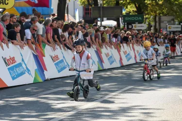 Kinder fahren mit Laufrädern in einem Wettkampf. Eine große Menge von Zuschauern schaut begeistert zu.