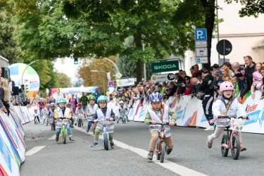 Eine Gruppe von Kindern fährt mit ihren Fahrrädern in einem Wettbewerb. Zuschauer stehen an der Strecke und verfolgen das Rennen.