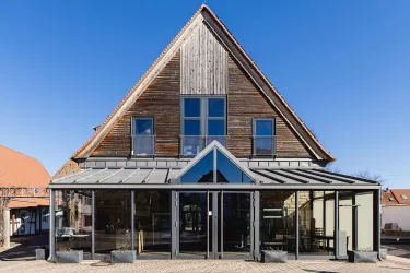 Ein modernes Gebäude mit einem Holzdach und großen Glasfenstern. Der Himmel ist klar und blau.