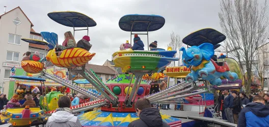 Ein bunter Karussell mit vielen Fahrgästen auf Fahrt. Menschen stehen um das Karussell herum und genießen die festliche Atmosphäre.