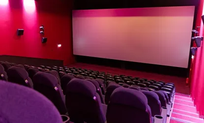 Ein modernes Kino mit roten Wänden und bequemen Sitzen. Die Leinwand ist groß und bereit für die nächste Vorstellung.