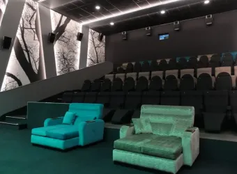Ein modernes Kinosaal mit bequemen Sofas und einer schlichten, eleganten Wandgestaltung. Die Umgebung ist dunkel gehalten, um ein optimales Kinoerlebnis zu bieten.