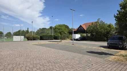 Ein großer Parkplatz mit vielen freien Stellplätzen. Im Hintergrund sind Bäume und ein Gebäude zu sehen.