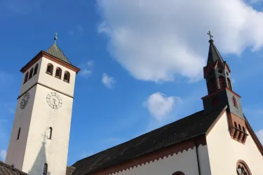 Eine Kirche mit zwei Türmen vor einem blauen Himmel. Die Architektur zeigt historische Elemente und macht einen einladenden Eindruck.