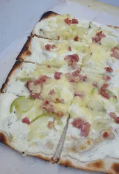 Eine frisch gebackene Flammkuchen mit Käse, Speck und dünn geschnittenen Äpfeln. Der Teig ist goldbraun und knusprig.