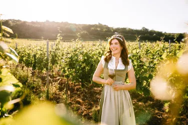 Eine fröhliche Frau steht in einem Weinberg. Die Sonne scheint und die Trauben wachsen in der Nähe.