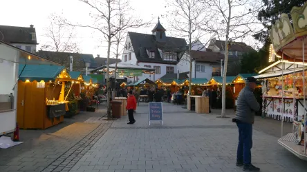 Ein gemütlicher Weihnachtsmarkt mit festlich dekorierten Ständen. Menschen schlendern durch die beleuchteten Stände und genießen die Atmosphäre.