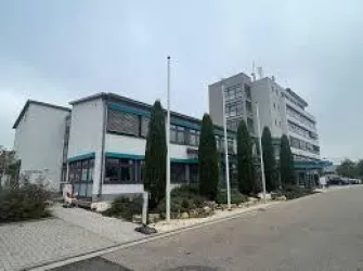 Ein modernes Bürogebäude mit mehreren Stockwerken und großen Fenstern. Im Vordergrund sind gepflegte Grünanlagen und ein Parkplatz zu sehen.