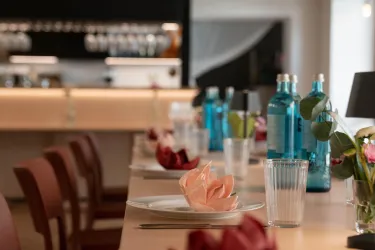 Ein elegant gedeckter Tisch mit Wasserflaschen und Blumen. Im Hintergrund ist eine moderne Bar zu sehen.