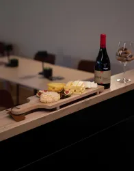 Eine Holzplatte mit verschiedenen Käsesorten und Feigen. Daneben steht eine Flasche Rotwein und ein Glas mit Snacks.