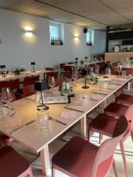 Ein elegantes Restaurant mit langen Tischen und roten Stühlen. Die Tische sind festlich mit Gläsern, Besteck und kleinen Pflanzen dekoriert.