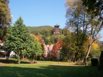 Eine malerische Landschaft mit bunten Herbstbäumen und einer kleinen Stadt im Vordergrund. Im Hintergrund ragt ein hoher Felsen hervor.