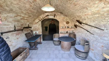 Ein historischer Raum mit einer gewölbten Decke aus Ziegelsteinen. Es gibt ein Tisch, Stühle und einige alte Werkzeuge an den Wänden.