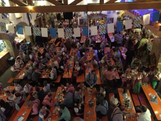 Eine lebendige Veranstaltung in einem festlich geschmückten Raum. Viele Menschen sitzen an langen Bänken und genießen die Atmosphäre.