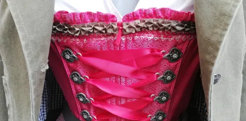 Ein traditionelles Dirndl in leuchtendem Pink mit versehenen Schnürungen. Es ist mit eleganten Details und einer passenden Bluse kombiniert.