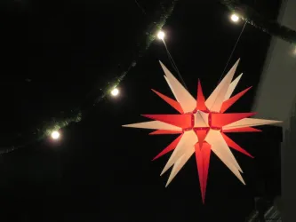 Ein großer, leuchtender Weihnachtsstern in Rot und Weiß hängt im Dunkeln. Sanftes Licht strahlt von ihm und schafft eine festliche Atmosphäre.