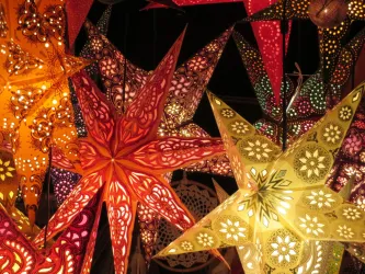 Bunte Papiersterne in verschiedenen Formen und Farben leuchten im Dunkeln. Die dekorativen Sterne schaffen eine festliche Atmosphäre.