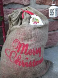 Ein großer Jutesack mit der Aufschrift "Merry Christmas". Der Sack ist festlich dekoriert und hat eine rote Schleife.