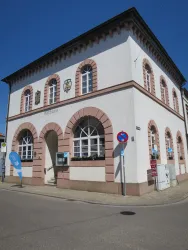 Ein historisches Gebäude mit einem auffälligen Fassadenstil und großen Fenstern. Es befindet sich an einer Straßenecke mit Verkehrsschildern in der Nähe.
