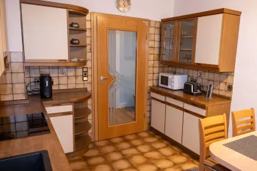 Eine moderne Küche mit Holzregalen und weißen Schränken. Sie enthält eine Mikrowelle, einen Wasserkocher und einen Tisch mit Stühlen.