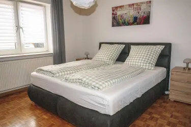 Ein gemütliches Schlafzimmer mit einem Doppelbett und karierten Bettdecken. Das Fenster lässt viel Tageslicht herein und es gibt einen modernen Nachttisch.