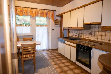 Eine helle Küche mit weißen Schränken und Holzdetails. Der Tisch steht neben den Fenstern und bietet viel Platz für gemeinsame Mahlzeiten.