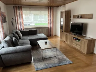 Ein modernes Wohnzimmer mit einem grauen Sofa und einem Holztisch. Neben dem Sofa steht ein Fernseher auf einem eleganten TV-Möbel.