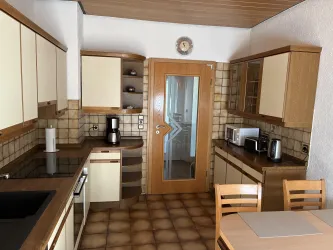Eine moderne Küche mit Holzregalen und hellen Schränken. Es gibt einen Tisch mit Stühlen und verschiedene Küchengeräte.
