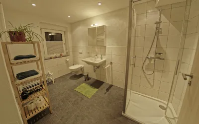 Ein modernes Badezimmer mit einer Dusche und einem Waschbecken. Es sind Handtücher und Pflanzen zur Dekoration vorhanden.