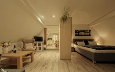 Ein modernes Dachzimmer mit Holzfußboden und einer gemütlichen Atmosphäre. Es enthält einen Bereich mit einem Bett, einem Tisch und einem Fernseher.