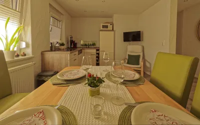 Ein einladender Essbereich mit einem Holztisch und grünen Stühlen. Auf dem Tisch sind gedeckte Teller und eine kleine Pflanze dekoriert.