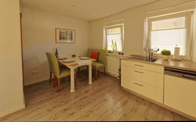 Eine helle Küche mit einem kleinen Essbereich. Der Tisch ist gedeckt und es gibt Pflanzen auf der Fensterbank.