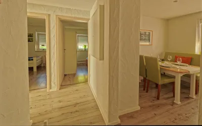 Ein heller Flur mit Zugang zu einem Wohnbereich. Auf der rechten Seite steht ein Esstisch mit Stühlen.