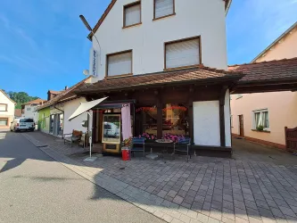 Ein charmantes Gebäude in einer ruhigen Straße. Vor dem Eingang stehen Tische und Stühle, und es gibt Blumen im Fenster.