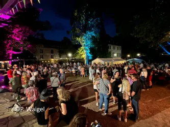 Eine lebendige Nachtveranstaltung mit vielen Menschen, die tanzen und sich amüsieren. Bunte Lichter beleuchten den Bereich und schaffen eine festliche Atmosphäre.