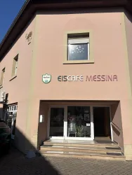 Ein Eiscafé namens Messina mit einer einladenden Eingangsfront. Das Gebäude ist in einem hellen Farbton gestrichen und hat große Fenster.