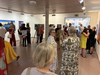 Eine lebhafte Kunstausstellung mit vielen Besuchern, die sich um die Bilder versammeln. Die Wände sind mit verschiedenen Kunstwerken geschmückt, während die Menschen angeregt miteinander sprechen.